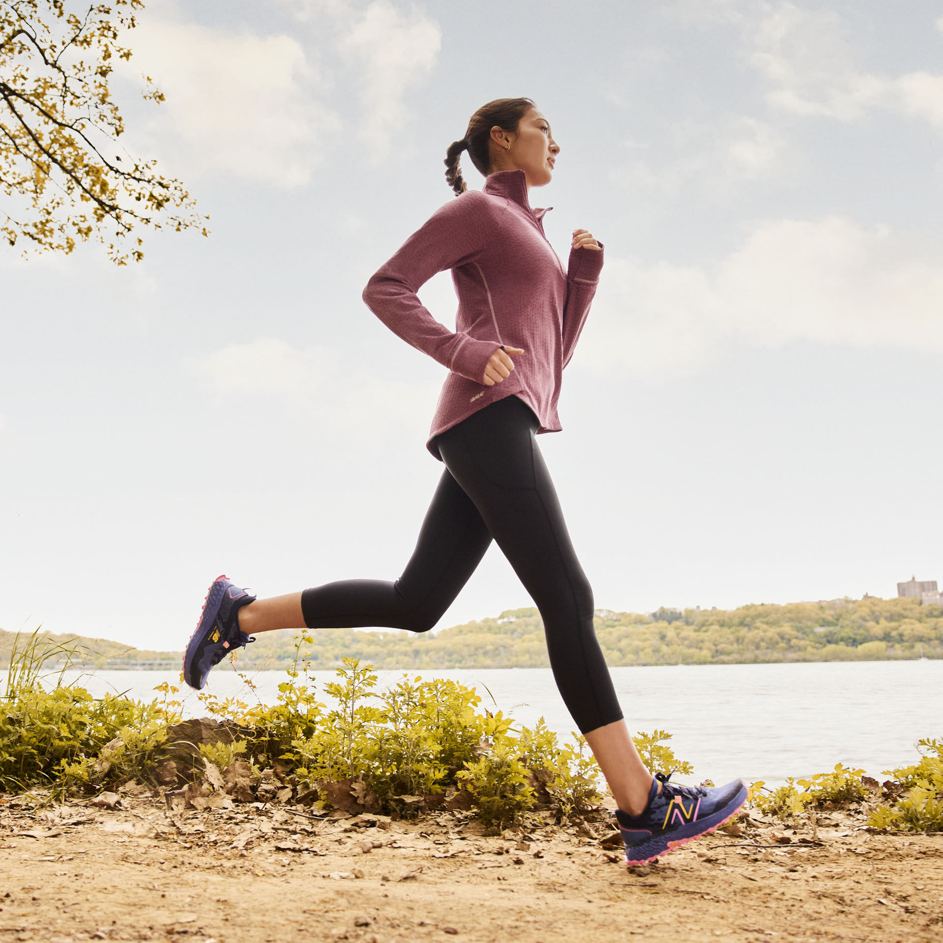 Woman running on dirt trail near lake wearing New Balance gear